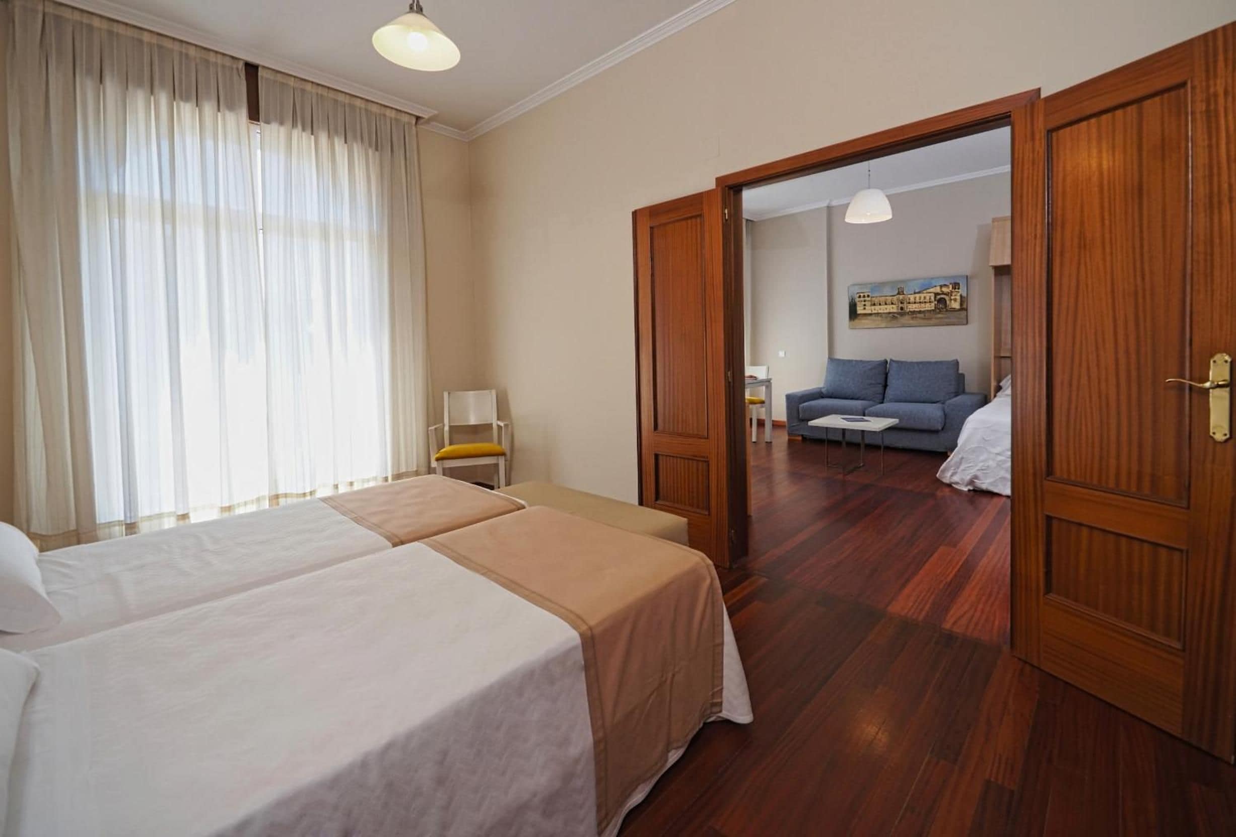 Ein Hotelzimmer mit zwei Betten, Holzboden, einer Sitzecke mit einer Couch und einem Gemälde an der Wand.