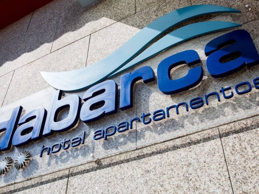 A sign for 'Dabarca Hotel Apartamentos' with a modern design and a wave-like graphic element.