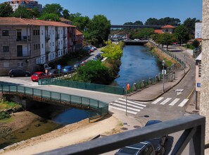 Un río atraviesa una ciudad con edificios a ambos lados, un puente peatonal y automóviles estacionados a lo largo de la calle.