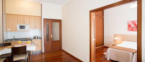 A compact hotel room with a bed, bedside table, and a view of the kitchen area.