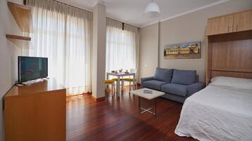 Una habitación de hotel con cama, sofá, televisión, escritorio con sillas y un cuadro en la pared.