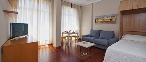 Una habitación de hotel con cama, sofá, televisión, escritorio con sillas y un cuadro en la pared.