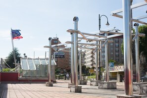 Una plaza urbana moderna con estructuras metálicas, un edificio de vidrio y un letrero de hotel.
