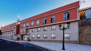 Un hotel con fachada roja, múltiples ventanas con balcones y un muro de piedra en un lateral.