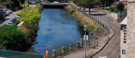 Ein Fluss fließt durch eine Stadt, mit einer Fußgängerbrücke, einem Parkplatz und einer Straße mit Zebrastreifen.