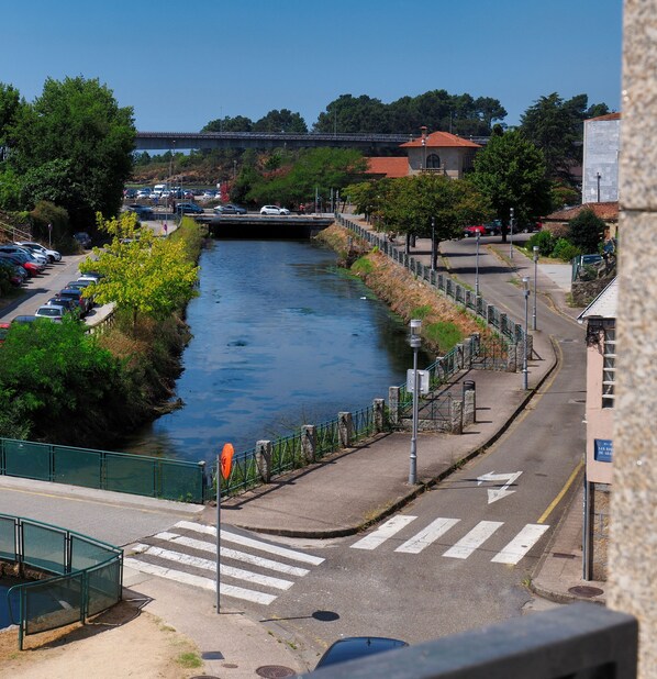 A river running through a city with a pedestrian bridge, a parking lot, and a road with a pedestrian crossing.
