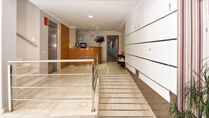 Un vestíbulo de hotel con una escalera de mármol, una recepción y casilleros.