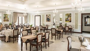 Un comedor espacioso con múltiples mesas y sillas, elegantes candelabros y obras de arte enmarcadas en las paredes.