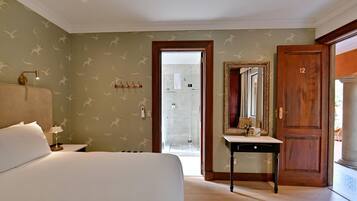 A hotel room with a bed, bedside table, lamp, mirror, and a door leading to a bathroom.