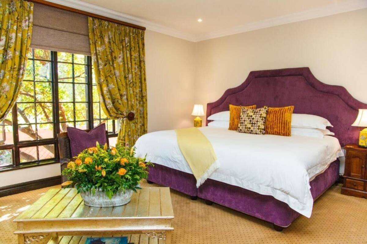 A bedroom with a large bed, a nightstand, a window with curtains, and a table with a flower arrangement.
