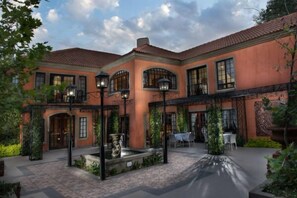 A courtyard with a fountain, outdoor seating, and a building with arched windows and a tiled roof. - Ivory Manor Boutique Hotel (Pretoria)