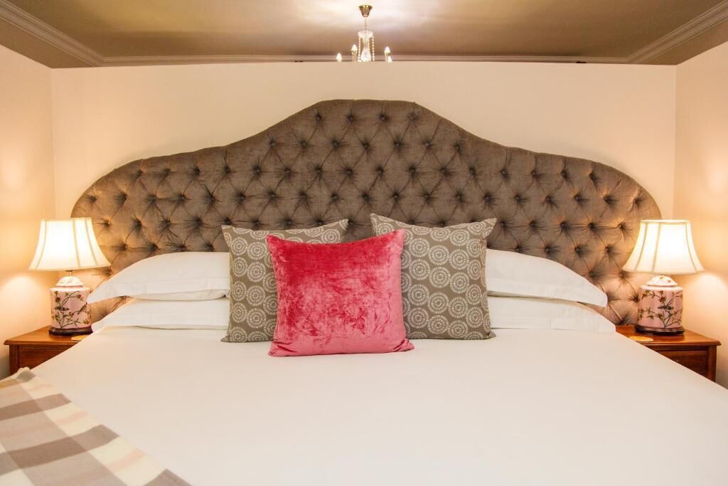 A bedroom with a tufted headboard, two bedside lamps, and a bed with white linens and patterned pillows.