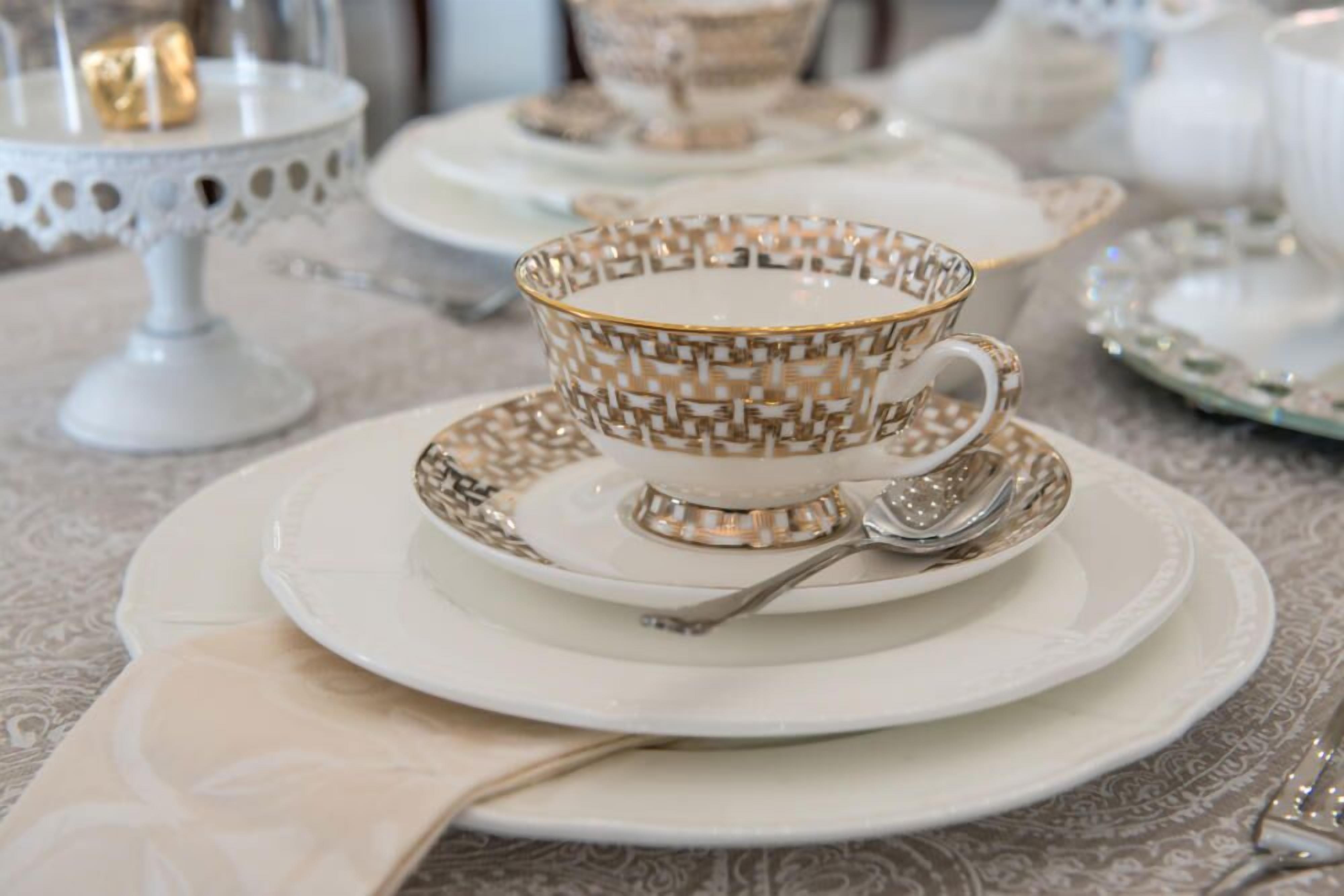 Uma mesa posta com porcelana requintada, incluindo uma xícara e pires, uma colher e uma chaleira.