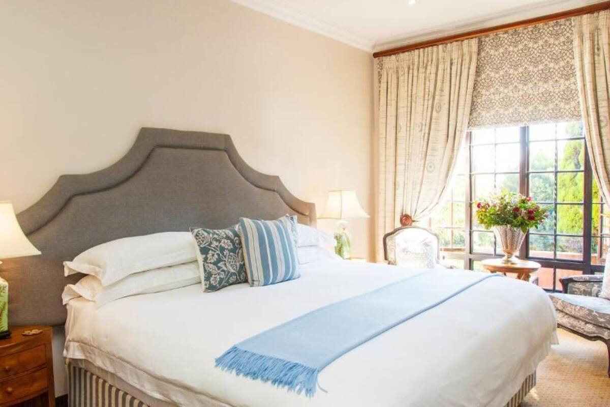 A neatly made bed with a grey headboard, white linens, and blue accents. There are two bedside tables with lamps and a vase of flowers.