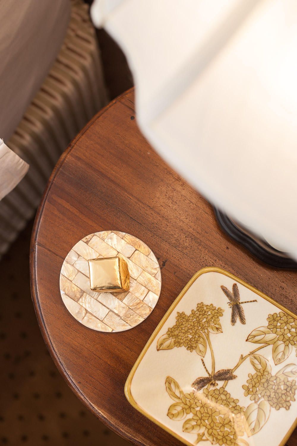 Una mesa de madera con una lámpara blanca, un plato decorativo con motivos florales y un posavasos de panal con un panal encima.