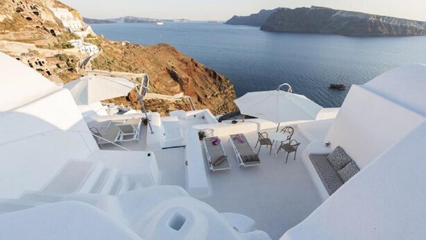 A white, modern outdoor seating area with a view of the sea and rocky landscape. - The Architect's Cave House (Santorini)
