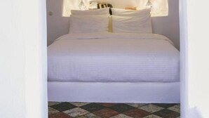 A bedroom with a white archway, a bed with white linens, and a patterned floor. - The Architect's Cave House (Santorini)