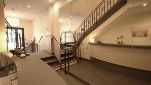 Un moderno vestíbulo de hotel con una escalera curva, un mostrador de recepción y un separador de vidrio.