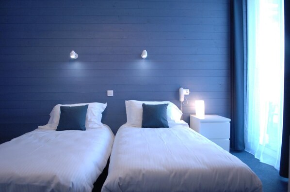 Habitación de hotel con dos camas, una mesita de noche y una lámpara.