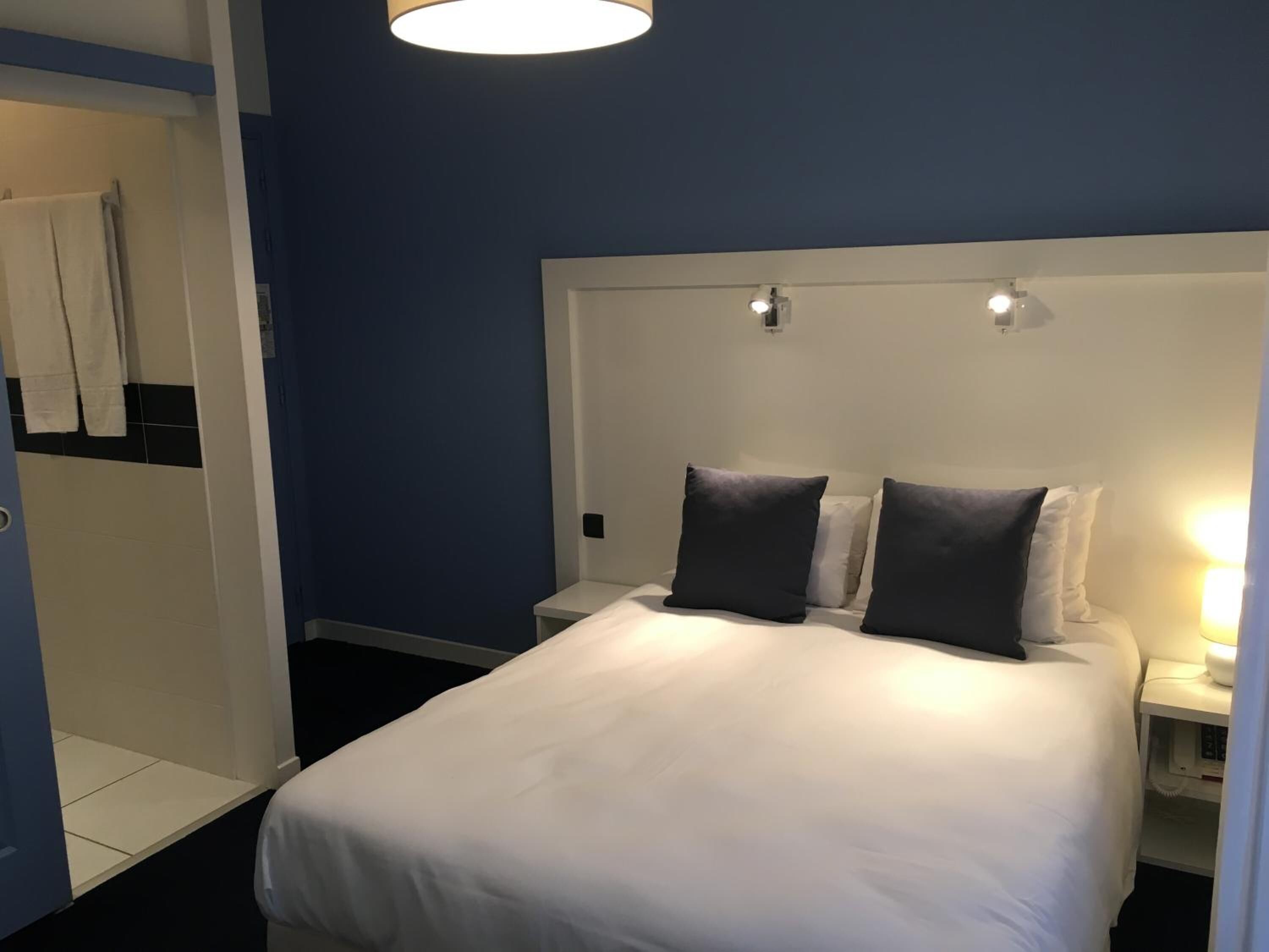 Une chambre d’hôtel avec un grand lit, deux tables de chevet, une armoire et un luminaire au plafond.
