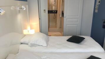 A hotel room with a bed, a bedside lamp, a door leading to a bathroom, and a wall-mounted phone.
