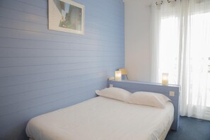 Ein Einzelbett mit weißer Bettwäsche in einem Zimmer mit blauen Wänden und einem Fenster mit weißen Vorhängen.
