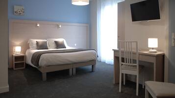 A hotel room with a bed, bedside tables, a desk with a chair, a TV, and a window with curtains.