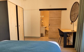 A bedroom with a bed, a desk, and a chair. There is a door leading to a bathroom.
