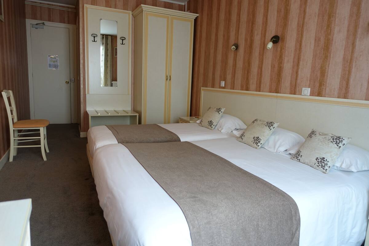 Une chambre d’hôtel avec deux lits, une armoire, une chaise et un miroir.