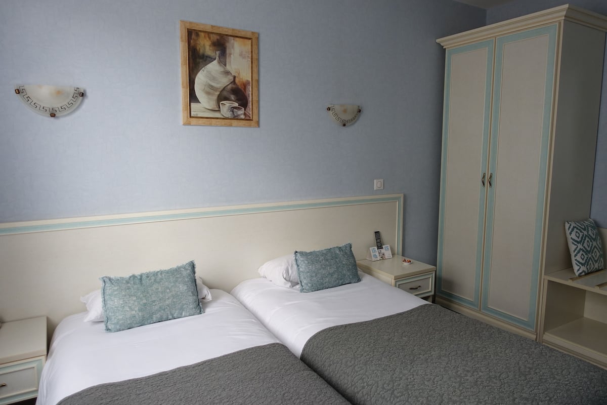 Une chambre avec deux lits, une armoire, une table de chevet et des lampes fixées au mur.