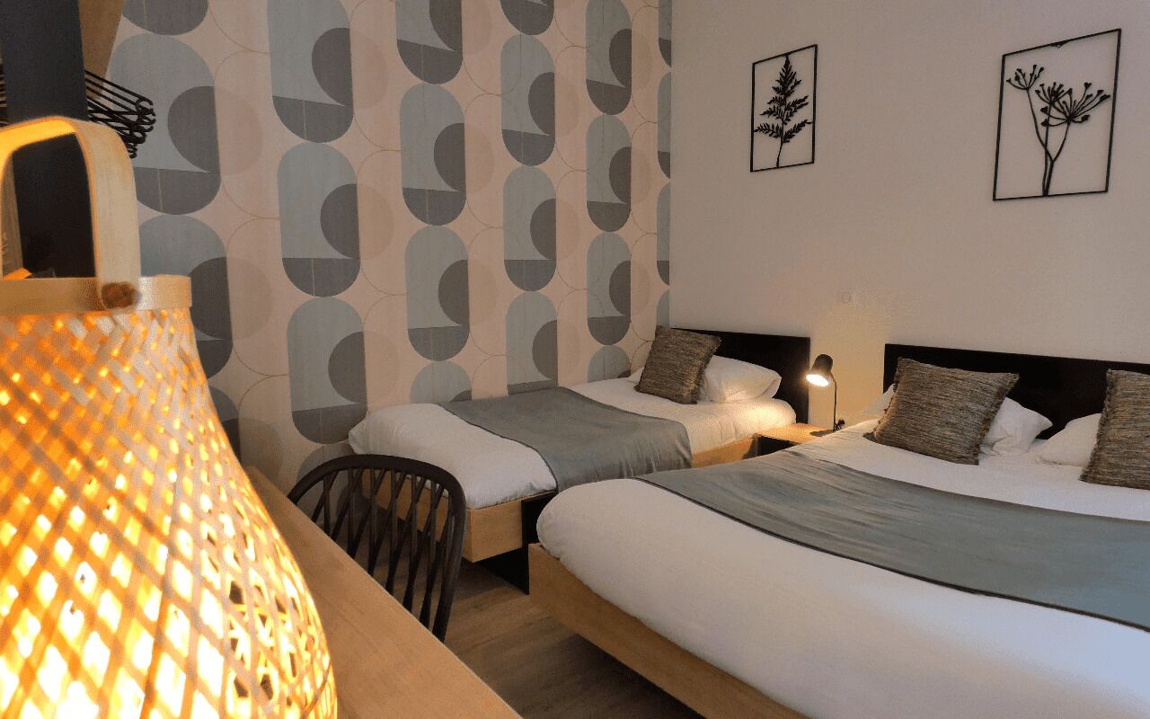 A hotel room with two beds, a nightstand, a lamp, and wall art.