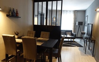 A modern living room with a dining area, featuring a large window, a sofa, a coffee table, and a TV on a stand.
