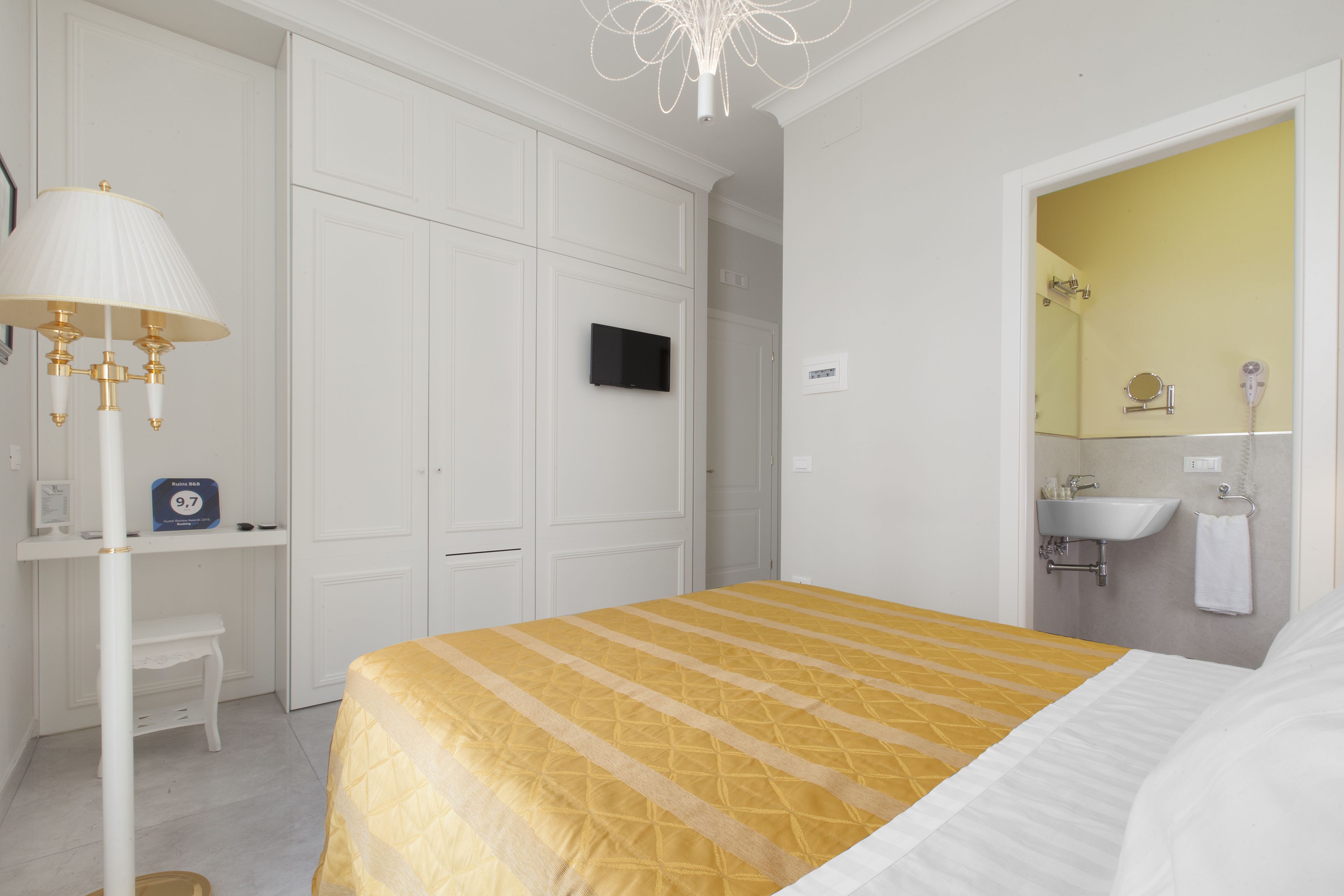 A hotel room with a bed, a desk, a television, and a bathroom with a sink and mirror.
