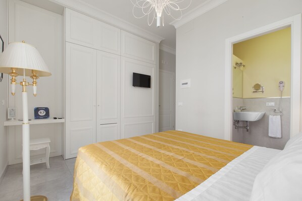 A hotel room with a bed, a desk, a television, and a bathroom with a sink and mirror. - Ruins B&B (Ercolano)