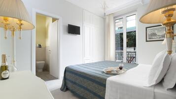 Habitación de hotel con cama, lámparas de noche, televisor, minibar y vistas al balcón.