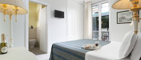 A hotel room with a bed, bedside lamps, a television, a minibar, and a balcony view.