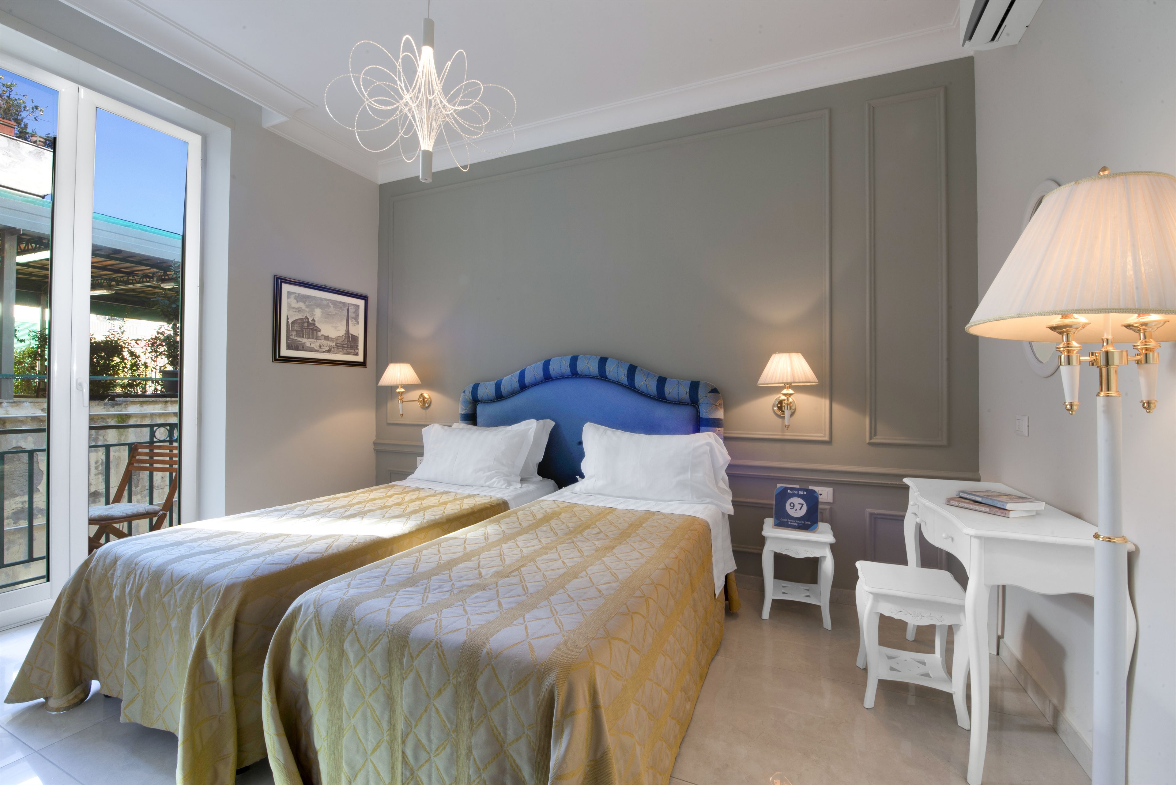A hotel room with two beds, a desk, and a chair. There is a window with a view of the outdoors.