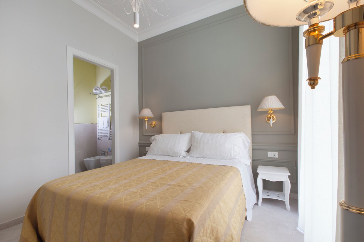 Un dormitorio ordenado con una cama grande, lámparas de noche y una mesita de noche pequeña.