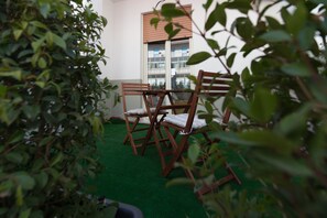A room with a green artificial turf floor, a wooden table with chairs, and a window with blinds.