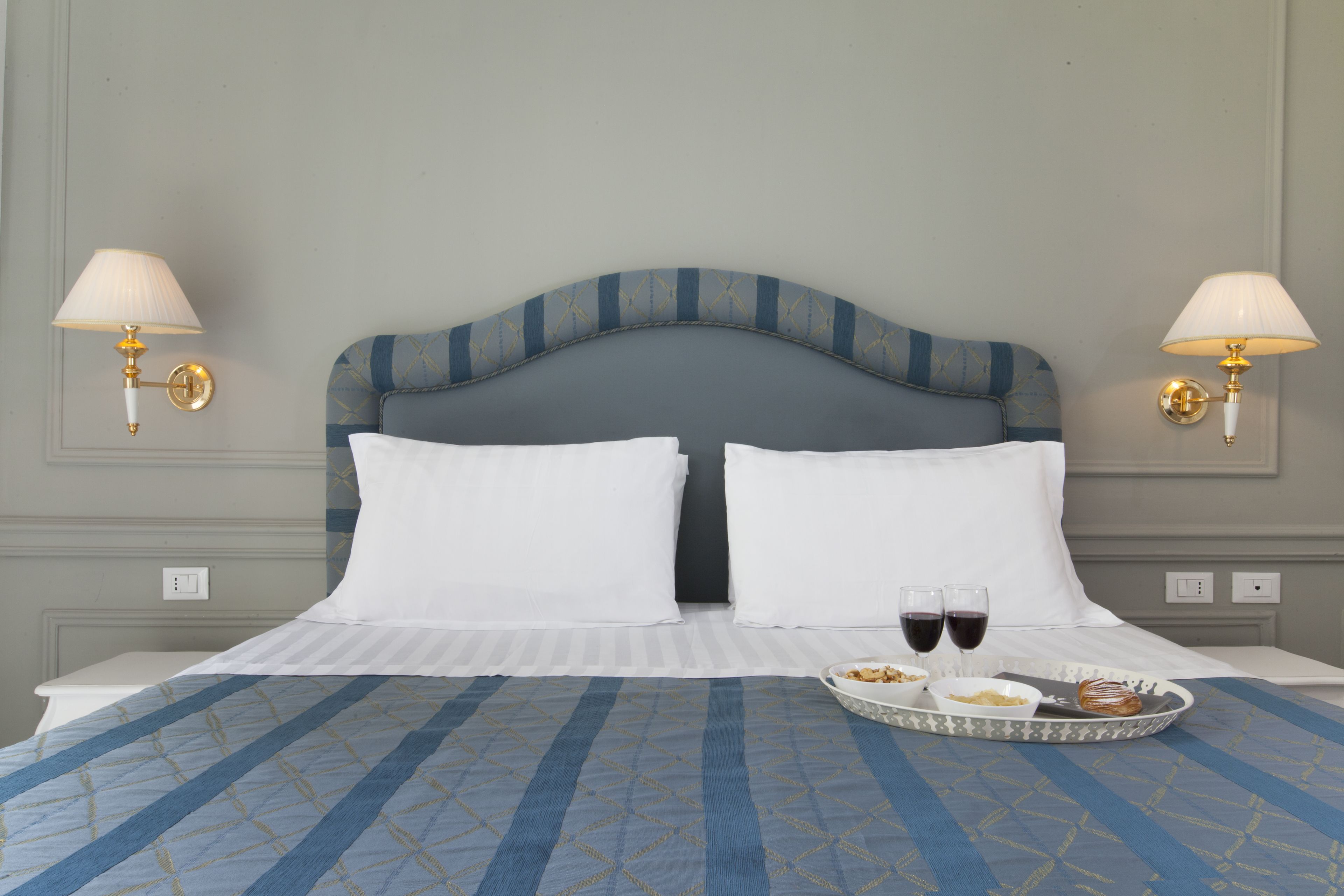 A neatly made bed with white linens, two wall-mounted lamps, and a tray with food and drinks on the bed.