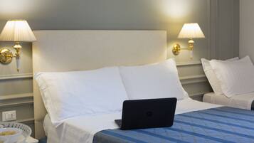 A hotel room with a bed, two bedside lamps, a laptop, and a bedside table with a bowl of fruit.