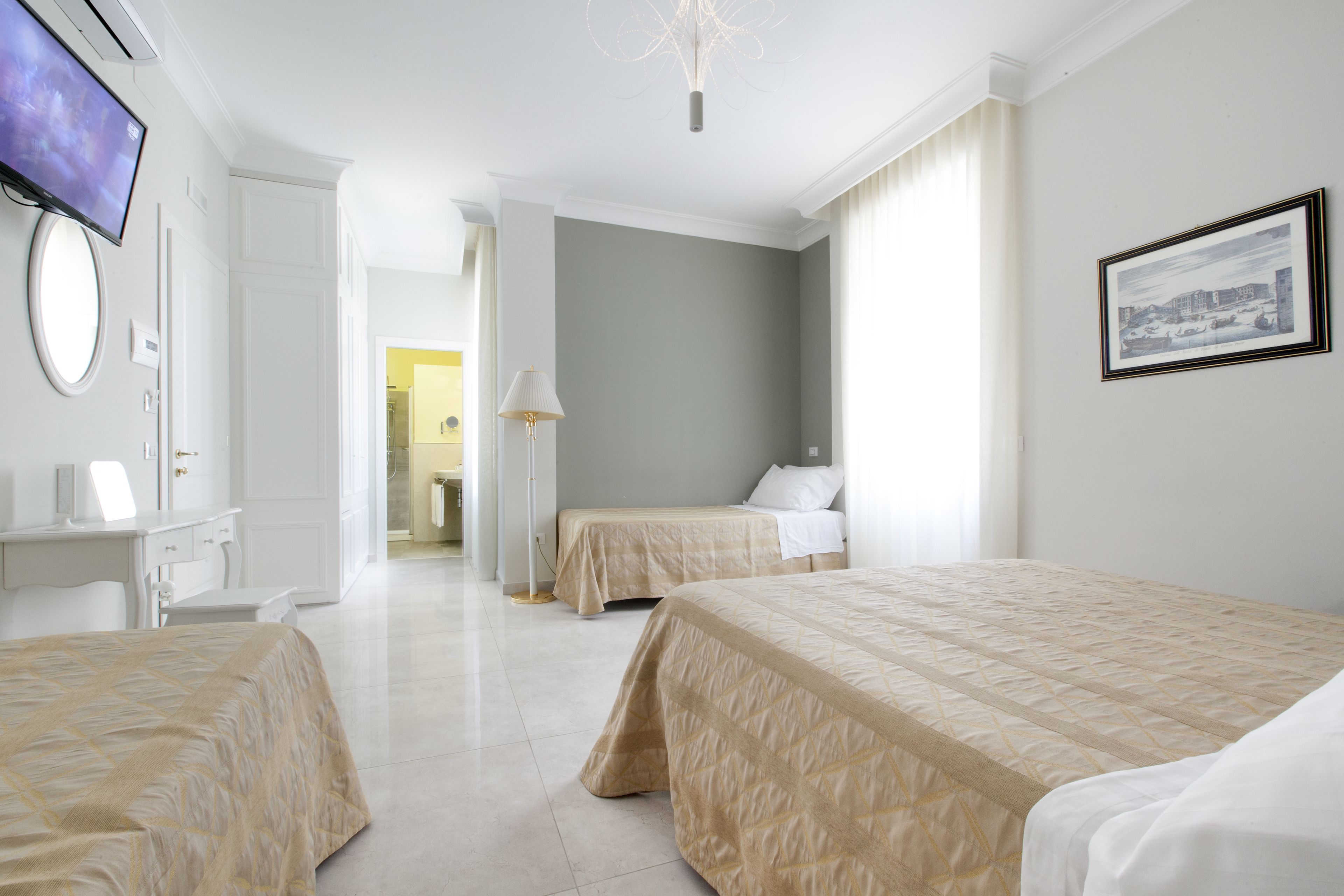 A hotel room with two beds, a desk, a TV, and a framed picture on the wall.