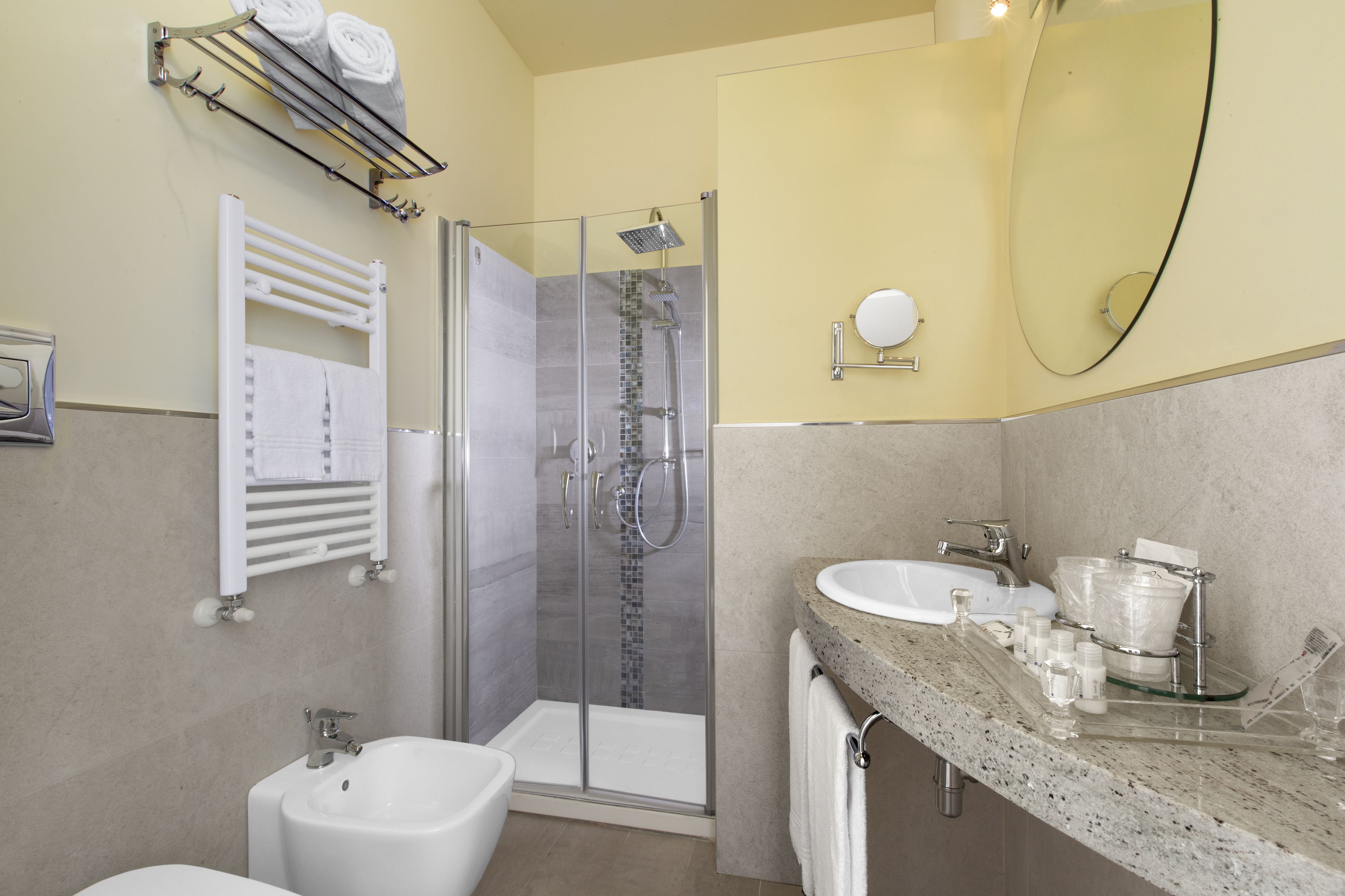 A modern bathroom with a glass-enclosed shower, a bidet, a sink with a marble countertop, and a towel rack with towels.