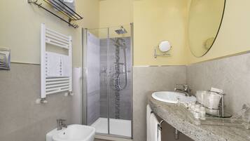 Une salle de bain moderne dotée d’une douche à parois de verre, d’un bidet, d’un lavabo avec un plan de travail en marbre et d’un porte-serviettes avec des serviettes.