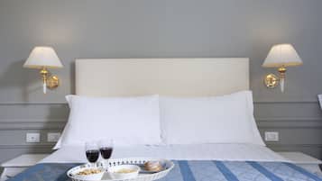Una habitación de hotel con una cama, dos lámparas de noche, una bandeja con aperitivos y dos copas de vino tinto.