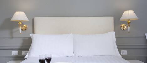 A hotel room with a bed, two bedside lamps, a tray with snacks, and two glasses of red wine.