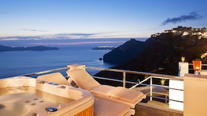 A balcony with a hot tub, lounge chairs, and a view of the sea and distant islands.