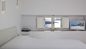 A minimalist bedroom with a large bed, a small bedside table, a TV, and a window with a view of the sea.