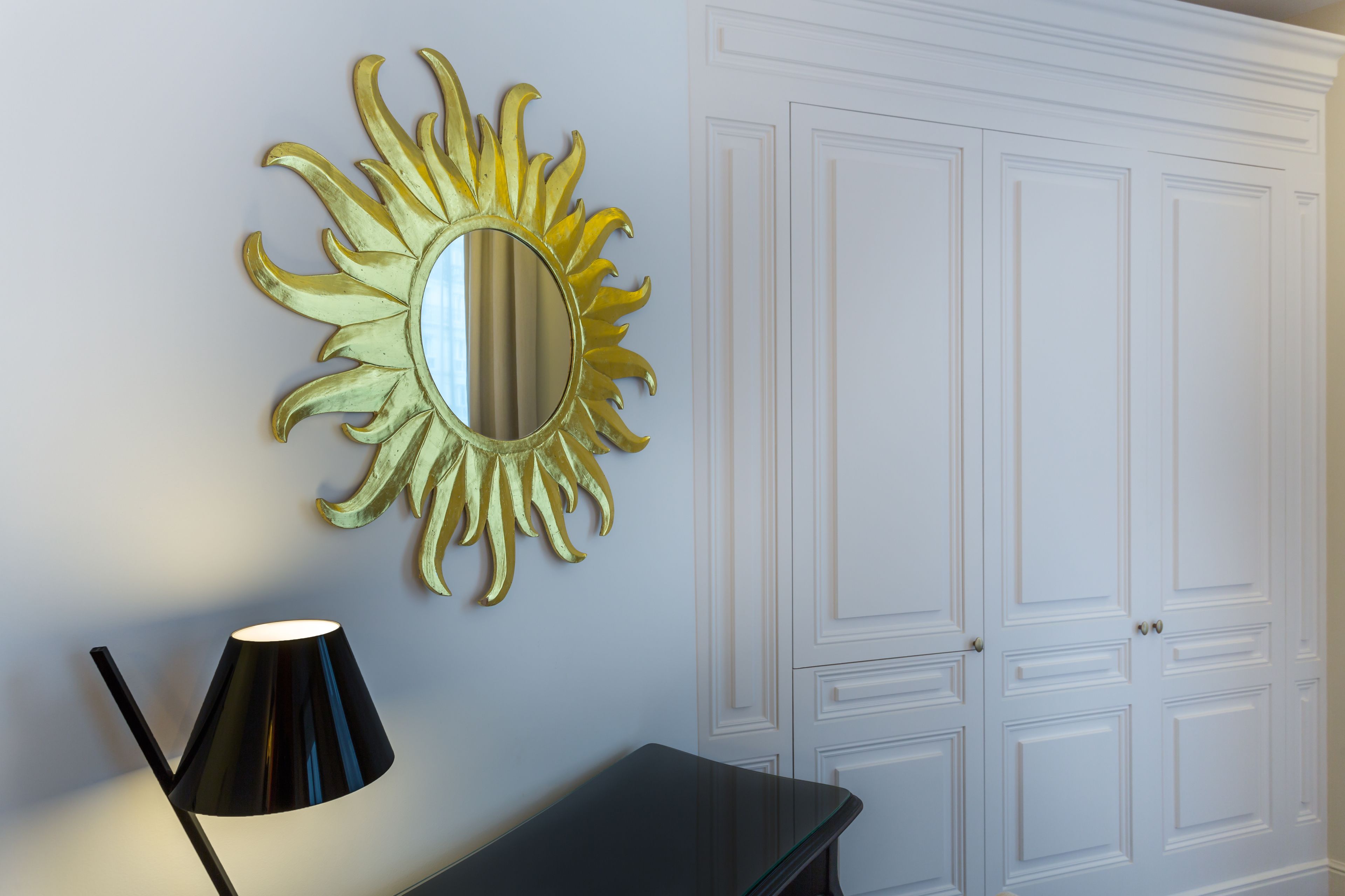 Une pièce avec un miroir fixé au mur, un lampadaire noir et une armoire blanche.