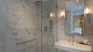 A modern bathroom with a glass-enclosed shower, a white sink with toiletries, and a large mirror.